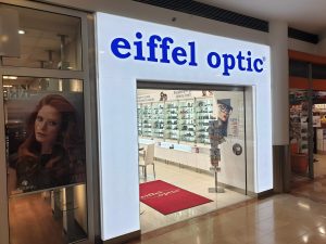 Světelná vstupní brána do obchodu eiffel optic, bílý rám, modrá svítící plexi písmena