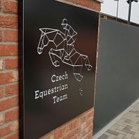 Černý světelný box s logem Czech Equestrian Team na cihlové zdi u vjezdu do areálu