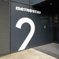 Bílé logo Metrostav, horní část písmena 2, černý plášť budovy