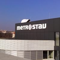 Bílé logo Metrostav lepené na černém plášti vrchní části budovy