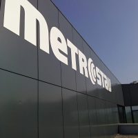 Bílé logo Metrostav lepené na černém plášti budovy, pohled zleva