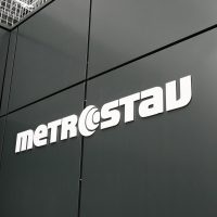 Bílé logo Metrostav lepené na černém plášti budovy, pohled zespoda