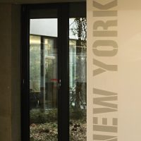 Svislý malovaný nápis NEW YORK na stěně chodby administrační budovy, skleněné dveře