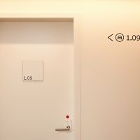 Bílá tabulka s černým označením dveří pokoje, šipka a navigace k pokojům na bílé stěně