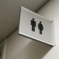 Informační výstrč v hliníkovém rámu na zdi, černý symbol muže a ženy, označení toalet