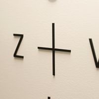 3D písmena S, Z, +, V, T, U, černé plexi lepené na bílé stěně