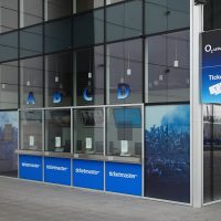 Pokladny s označením A, B, C, D, a loga ticketmaster, prodej vstupenek do O2 Universum, světelná výstrč na rohu prosklené budovy