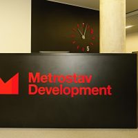 Černý recepční pult, červené 3D logo Metrostav Development, červeno-bílé hodiny na černé stěně