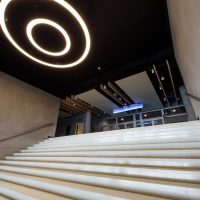 Osvětlené schodiště do patra O2 Universum, stropní svítidlo ve tvaru dvou soustředných kruhů, nerezová zábradlí, světelná výstrč