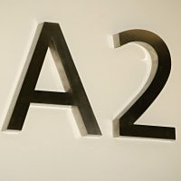 3D písmena A2 vyfrézovaná ze stříbrného hliníku s plechovými boky, připevněné distančními trny na bílé zdi