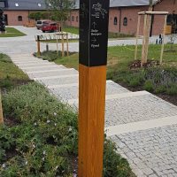 Navigační totem v areálu Czech Equestrian Team, gravírovaný černý matný dibond na lakovaném trámu, dlážděné schody a cesty