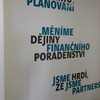 Modré a černé slogany Partners z plotrové folie nalepené na bílé zdi, zelené rostliny na podlaze