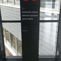 Černý kovový sloupek s červeným označením C3 a bílým textem jako navigací k oddělením, skleněné okno v černém rámu