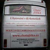 Zezadu vyfocený stříbrný autobus, na okně polep - vlevo fotka chaty a vpravo nápis červený Chata JITKA, pod oknem červené nápisy a piktogramy, dole červeně web a pod ním černý nápis AUTOBUSOVÁ DOPRAVA, telefon, dole spz, ve tmě