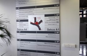 Stříbrná informační tabule s černými nápisy označení pater a firem, uprostřed orientační plán budov komplexu Plzeňský vědecko Technologický Park
