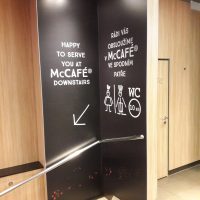 Laminovaná fototapeta s informačním značením uvnitř McCafé, nalepená na rohové stěně nad schody