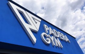 Bílý 3D nápis a logo Padera Gym na modré fasádě budovy