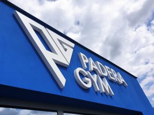 Bílý 3D nápis a logo Padera Gym na modré fasádě budovy