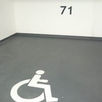 Emotikon handicapované osoby na podlaze jako malované značení parkovacího místa, číslo 71 a informační tabulka na stěně