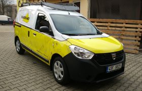 Auto Dacia Dokker polepené folií, spodní část žlutá s motivem technického výkresu, kabina a nástavba bílá, na zemi zámková dlažba