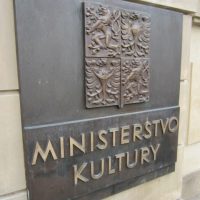 Bronzová deska s reliéfem státního znaku a nápisem MINISTERSTVO KULTURY, na pískově žluté fasádě budovy