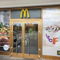 Reklamní označení vstupu do MC Donald's, 3D žluté logo nad skleněnými dveřmi, polep výlohy barevnou samolepicí okenní folií