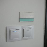 Navigační stříbrno-zelený štítek s gravírovaným značením 921, nalepeno na bílé zdi nad vypínači