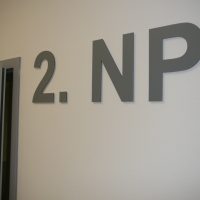 Šedý plastický 3D nápis 2. NP na bílé zdi vedle šedého rámu dveří, označení druhého podlaží budovy