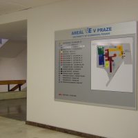 Orientační plán areálu VŠE v Praze na šedé informační tabuli, přimontováno na bílé zdi chodby, část schodiště