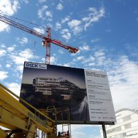 Instalace reklamního billboardu DOCK, pohled zespodu, vepředu detail vysokozdvižné plošiny, v pozadí jeřáb Metrostav