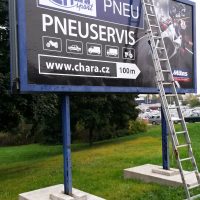 Instalace samolepicích folií na reklamní billboard, opřený žebřík, betonové podstavce na trávníku