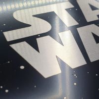 Detail bílého gravírovaného loga STAR WARS na kompozitní dibond desce v černé barvě s bílými tečkami