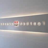 Obdélníková stříbrná podsvícená dibondová deska, černo-červené svítící logo Bohemia Medical, uchyceno na šedé zdi