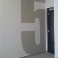 Malovaná šedá číslovka 5 přes celou výšku bílé stěny jako značení uvnitř interiéru, šedá podlaha, část dveří