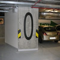 Černá číslovka 0 malovaná na šedém sloupu jako značení uvnitř podzemní garáže, dopravní zrcadlo, zaparkované automobily