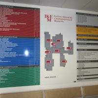 Velký orientační modulový systém IKEM, uprostřed plán budovy, po stranách značení částí, přimontováno na bílé zdi chodby