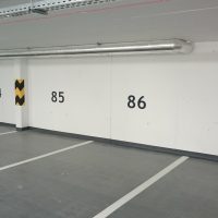 Označení parkovacích míst černými číslovkami malovanými na zdi, parkovací místa vyznačená bílými linkami na podlaze