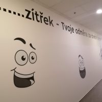 Černý slogan a kreslené stylizované obličeje řezané z plotrové folie nalepené na bílé zdi