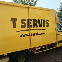 Z boku vyfocené žluté nákladní vozidlo, na skříni vozidla velký černý nápis T SERVIS a webová stránka www.tservis.com, v exteriéru na parkovišti