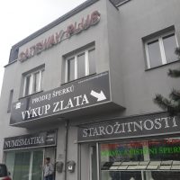 Černé folie nalepené na šedé fasádě budovy, bílé reklamní nápisy a šipka, 3D červené logo GATEWAY PLUS na budově