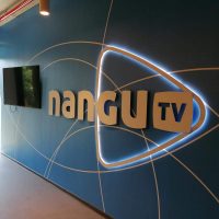 Podsvícené 3D logo Nangu TV na fototapetě s geometrickými motivy nalepené na zdi, televize