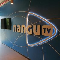 Podsvícené 3D logo Nangu TV na fototapetě s geometrickými motivy nalepené na zdi, televize