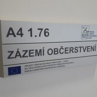 Dveřní štítek ze tří modulů, označení ZÁZEMÍ OBČERSTVENÍ Pražského vědecko technologického parku, přišroubováno na bílé stěně