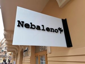 Nesvětelná reklamní výstrč Nebaleno na stěně budovy, černý 3D text, mléčné sklo, pískově žlutá fasáda