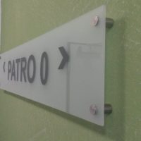 Detail skleněného panelu s šedým označením PATRO O, připevněného distančními šrouby na strukturované zdi