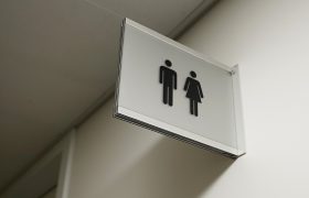 Skleněná navigační výstrč s černými piktogramy panáčků WC muži a ženy na bílé stěně
