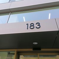 3D označení popisného čísla administrační budovy 183, černé plexi lepené na fasádě mezi vchodem a oknem prvního patra